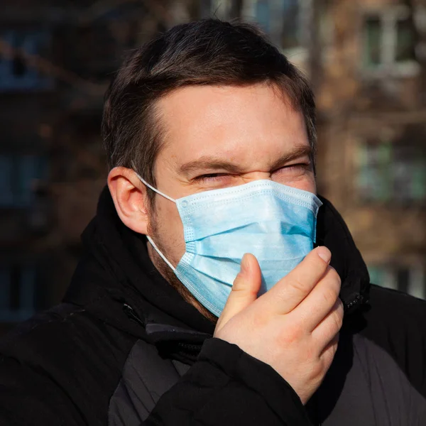 Virus covid-19. A man in a medical mask sneezes and coughs on a street in a city in Europe, protects against coronavirus