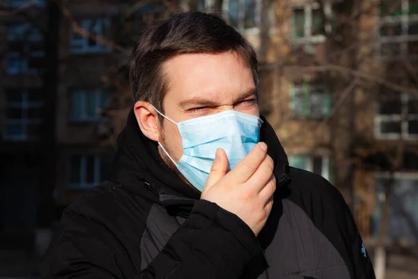 Virus covid-19. A man in a medical mask sneezes and coughs on a street in a city in Europe, protects against coronavirus