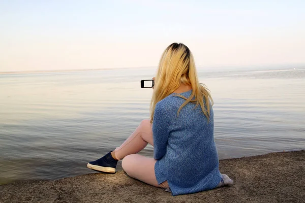 Gadis muda difoto di ponsel duduk di pantai o — Stok Foto