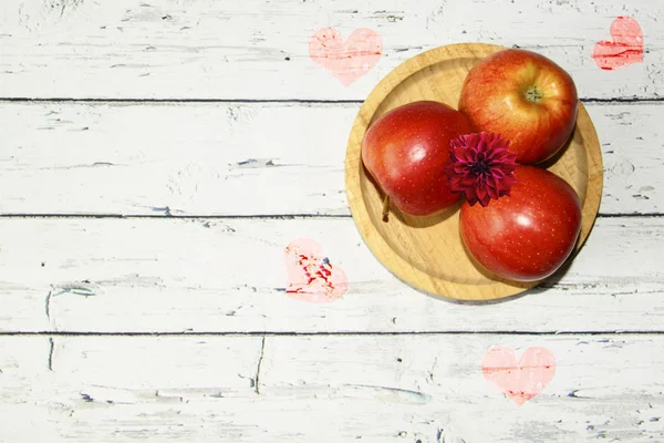 Manzanas rojas en un plato de madera en una mesa redonda con corazones, superior v — Foto de Stock