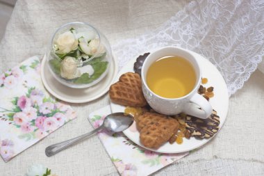 Beyaz fincan yeşil ışık ile kek kuru üzüm, çikolatalı kurabiyeleri pembe Çiçekli Dantel peçete üzerinde eski püskü şık zarif geleneksel iç.