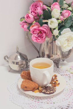 Beyaz fincan yeşil ışık ile kek kuru üzüm, çikolatalı kurabiyeleri pembe Çiçekli Dantel peçete üzerinde eski püskü şık zarif geleneksel iç.