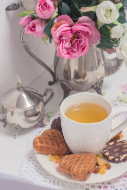 Beyaz fincan yeşil ışık ile kek kuru üzüm, çikolatalı kurabiyeleri pembe Çiçekli Dantel peçete üzerinde eski püskü şık zarif geleneksel iç.