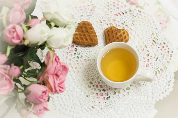 Tasse blanche de thé vert clair avec des gâteaux raisin, biscuits au chocolat dans shabby chic élégant intérieur traditionnel sur une serviette en dentelle avec des fleurs roses . — Photo