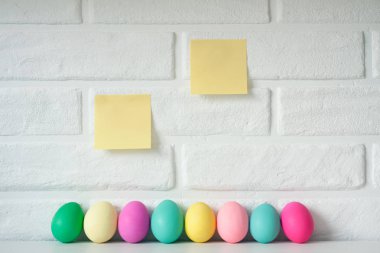 Paskalya yumurta yapışkan not kağıdı beyaz tuğla duvar arka plan ile renkli. Şirin Paskalya kutlamaları dekorasyon. 