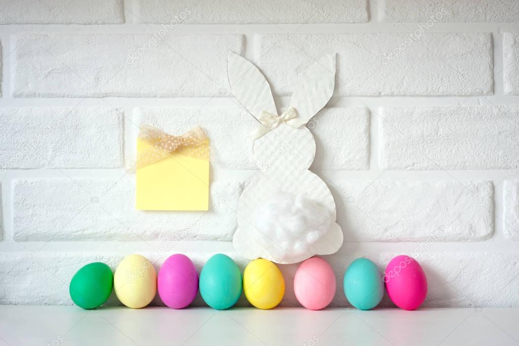 Easter colored eggs put in line on table against white brick wall background. Cute Easter celebration decor.