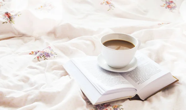 Still-life coffee cup and a book in bed on floral bed sheets — Stock Photo, Image