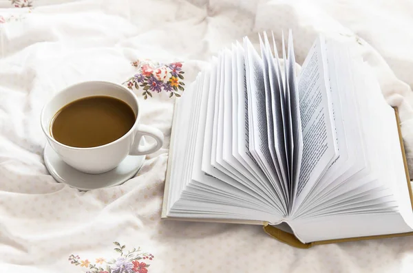 Stilleben kaffekopp och en bok i sängen på blommiga lakan — Stockfoto