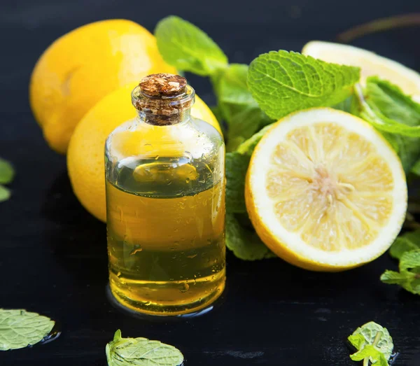 Botella de aceite esencial de limón con limones frutis y hojas de menta — Foto de Stock