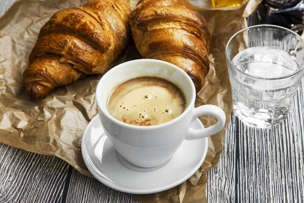 Šálek kávy s croissanty housky a vodního skla, ranní snídani — Stock fotografie