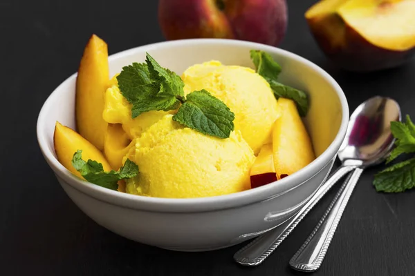 Cuillères de sorbet pêche dans un bol avec tranches de pêche et menthe — Photo