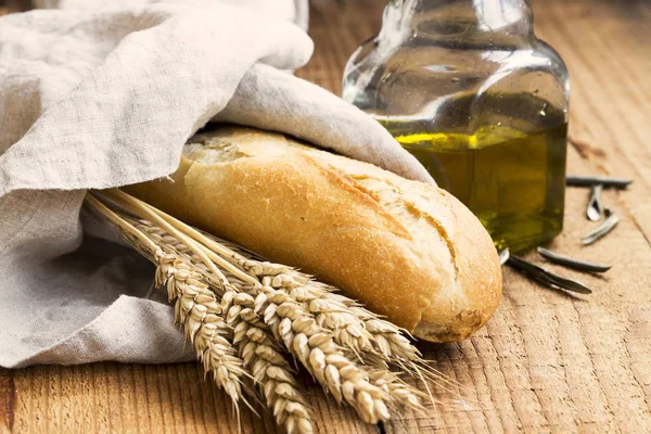 Baguette bread in linen towel with olive oil and ears of wheat