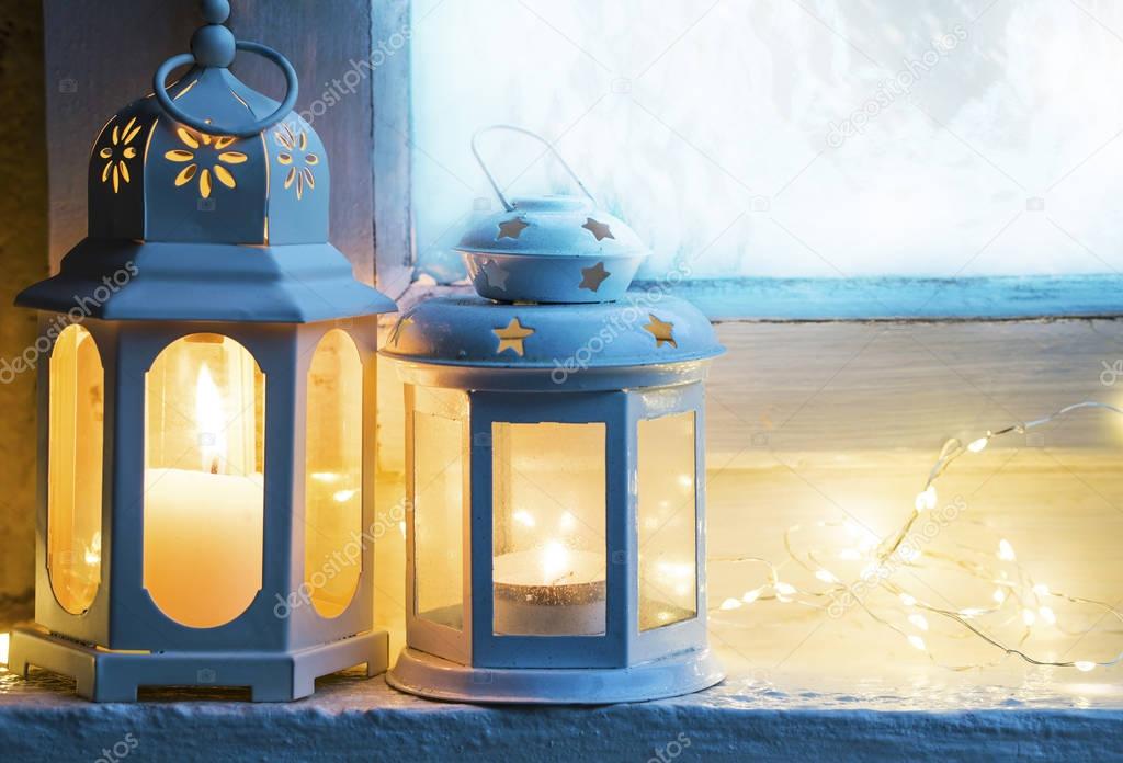 Christmas lanterns placed at the frozen window with burning cand