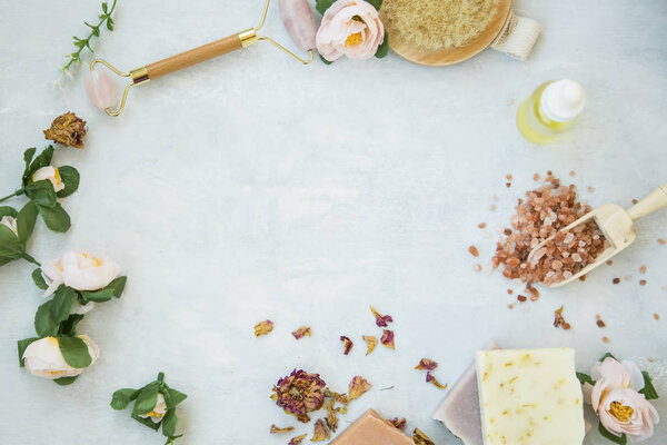 Spa still life frame with natural beauty products, bath salt, roses, natural soap, oil bottle, quartz face roller with copy space