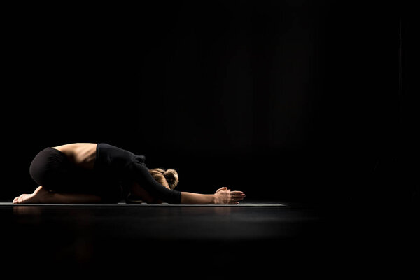 Woman performing Balasana or Childs Pose on yoga mat isolated on black
