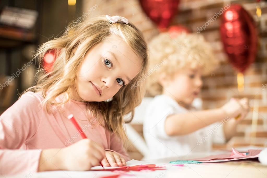 Beautiful little girl drawing at the table with red pen