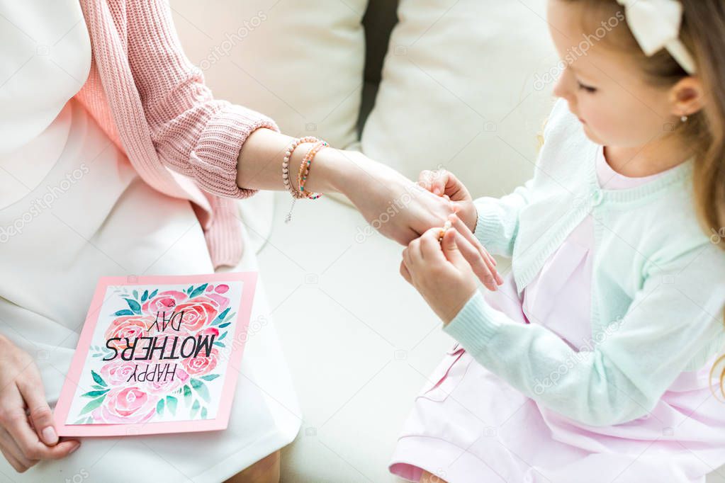 Girl putting jewelry on mother 