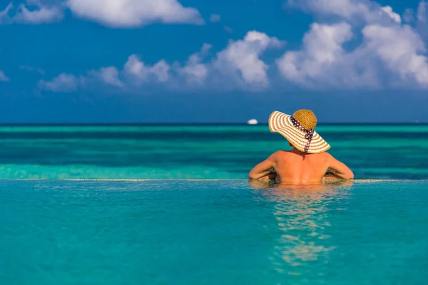 Sexy belle femme dans un chapeau relaxant par le ciel de la piscine avec du soleil et des nuages en arrière-plan — Photo
