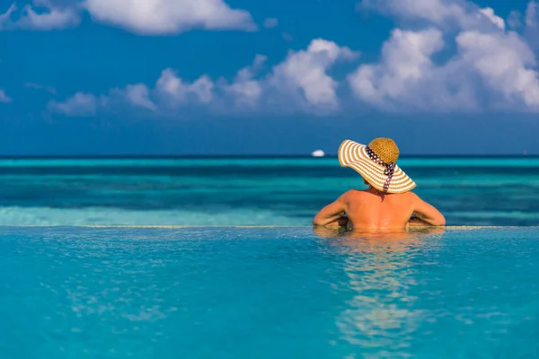 Mulher bonita sexy em um chapéu relaxante pelo céu da piscina com sol e nuvens no fundo — Fotografia de Stock