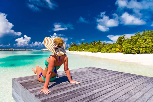 Молодая стройная женщина, лежащая на пирсе, тропический пляж, голубая вода и небо, солнечная, загорелая кожа, бикини, сексуальное тело, загорание, тропический отдых, расслабление. Летний отдых — стоковое фото