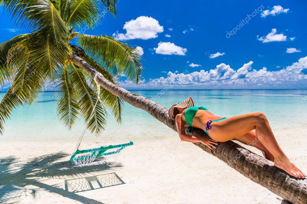 Young slim woman laying on tropical beach, blue water and sky, sunny, tanned skin, bikini, sexy body, sunbathing, tropical vacation, relaxing. Summer travel background