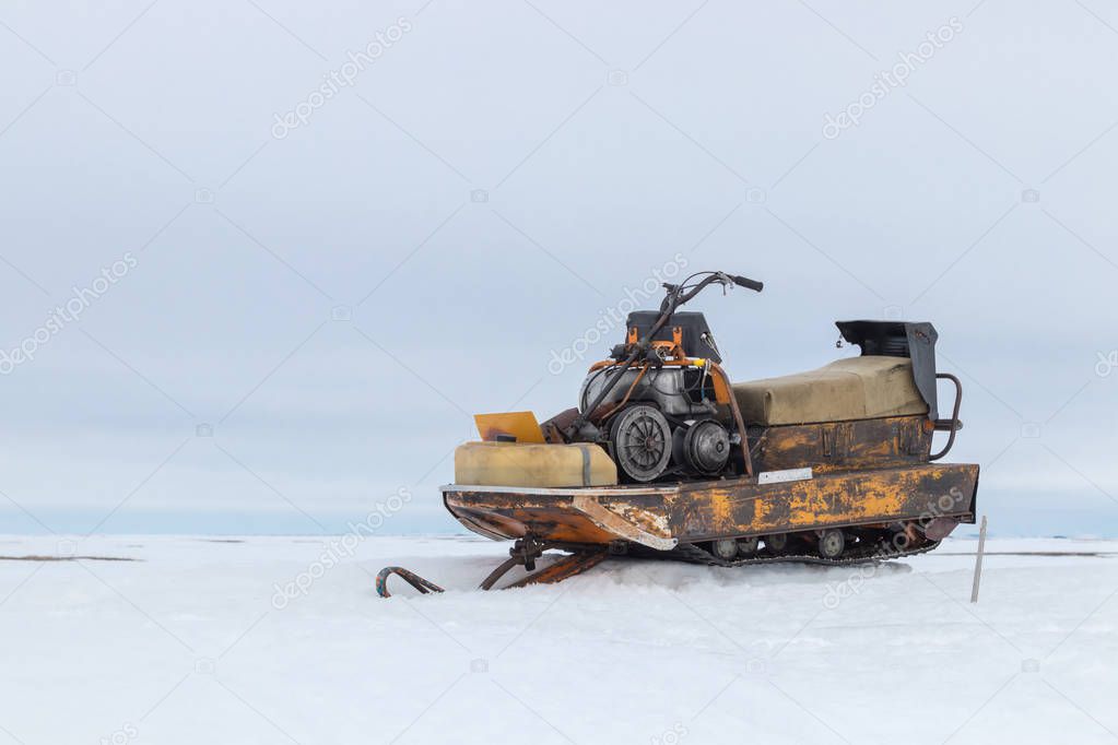 Photo of an old snowmobile standing in the snow in the tundra