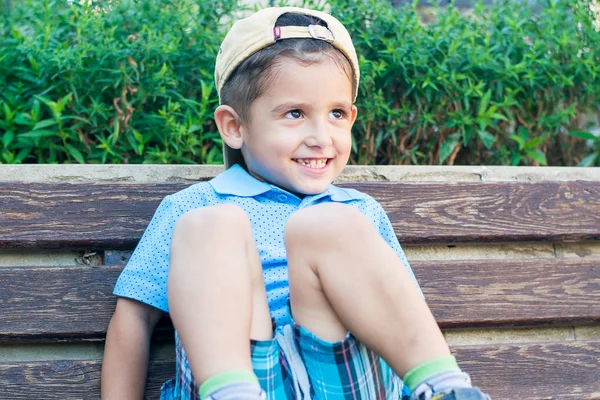 Little boy sitting on a bench with knees raised — Stock Photo, Image