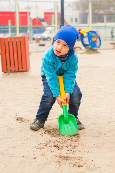 Мальчик с карими глазами играет с лопатой на детской площадке — стоковое фото
