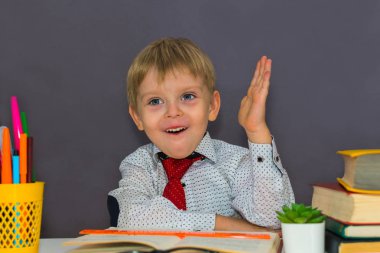 Anaokulu çocuğu elini gri bir B 'ye kaldırmış bir masada oturuyor.