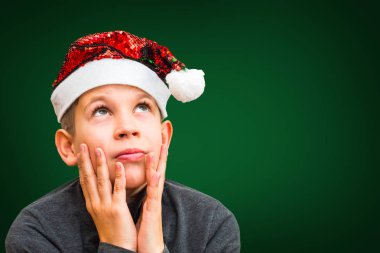 Yeşil arka planda Noel Baba şapkalı genç çocuk.