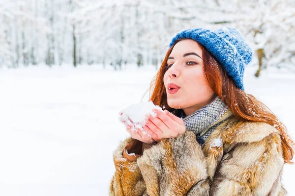 Encantadora jovem mulher em azul chapéu de malha soprando na neve — Fotografia de Stock