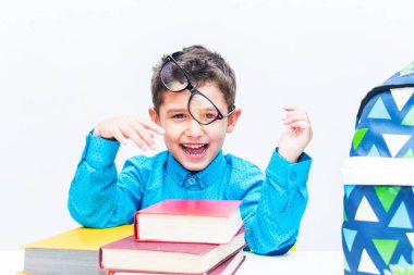 Masasında kitapları olan gözlüklü neşeli bir çocuk.