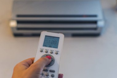 Bir kadının elindeki klimanın uzaktan kumandası.