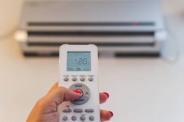 Bir kadının elindeki klimanın uzaktan kumandası.