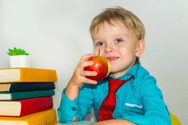 Un niño de preescolar en el escritorio comiendo una manzana. snack durante las clases. —  Fotos de Stock