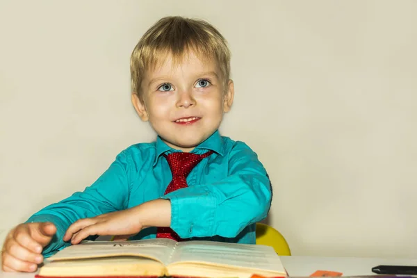 テーブルの上で本を読んで笑顔の就学前の少年 — ストック写真