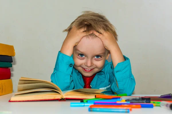 Silly boy sitting at a Desk with books. — Stock Photo, Image