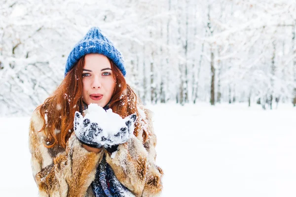 Encantadora jovem mulher em azul chapéu de malha soprando na neve. activo — Fotografia de Stock