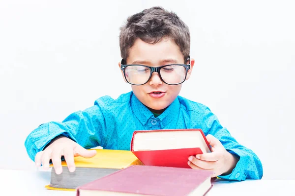 Söt pojke i glasögon sitter vid ett skrivbord med böcker — Stockfoto