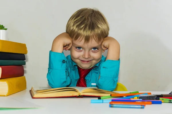 Silly boy sitting at a Desk with books. — Stock Photo, Image