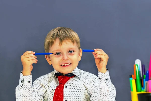 Cheerful boy sitting at a table on a gray background. preschoole Stock Picture