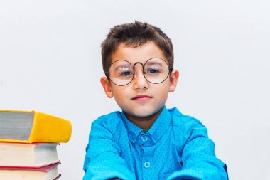 Gözlüklü sevimli çocuk elinde kitaplarla masada oturuyor.