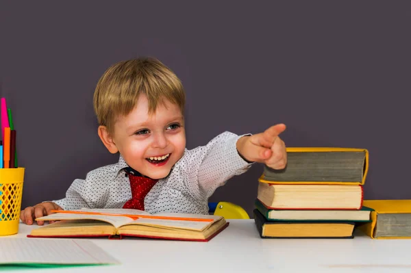 Glad Pojke Vid Ett Bord Med Böcker Pekar Med Fingret — Stockfoto