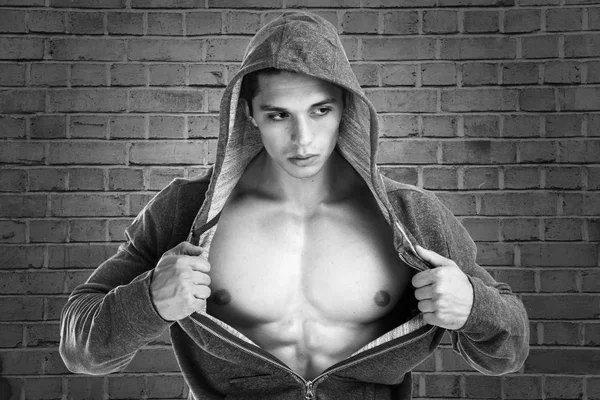 Bodybuilder sterke gespierde jongeman hoodie spieren bakstenen muur — Stockfoto