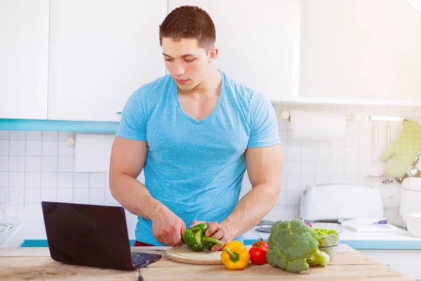 Hombre joven cocina comida saludable verduras ordenador internet eati — Foto de Stock