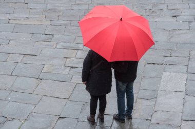 Couple holding red umbrella in a rainy day