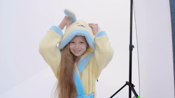 Onherkenbare vrouw het nemen van foto 's van schattig meisje met konijn badjas tijdens fotoshoot tegen witte achtergrond — Stockvideo