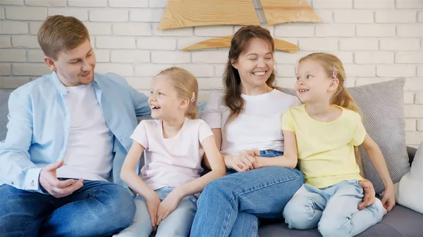 Yetişkin anne ve iki küçük kız gülümseyerek ve kanepede otururken ve evde büyüleyici bir hikaye dinlerken baba bakıyor