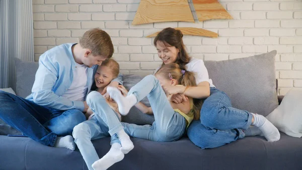 Homme et femme adultes chatouillant jumeaux assis sur un canapé confortable et s'amusant ensemble à la maison Photos De Stock Libres De Droits