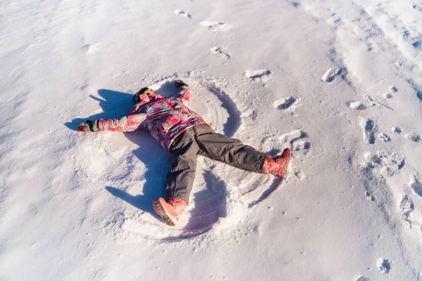 children lying on white snow in bright sunshine and making snow angels